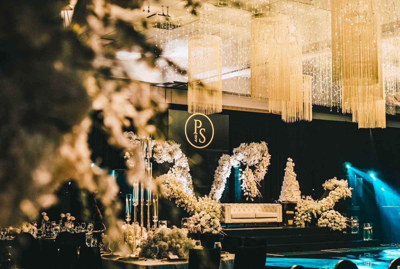 Opulent wedding reception with cascading string-light chandeliers, floral stage, and a monogrammed backdrop produced by Amped Entertainment