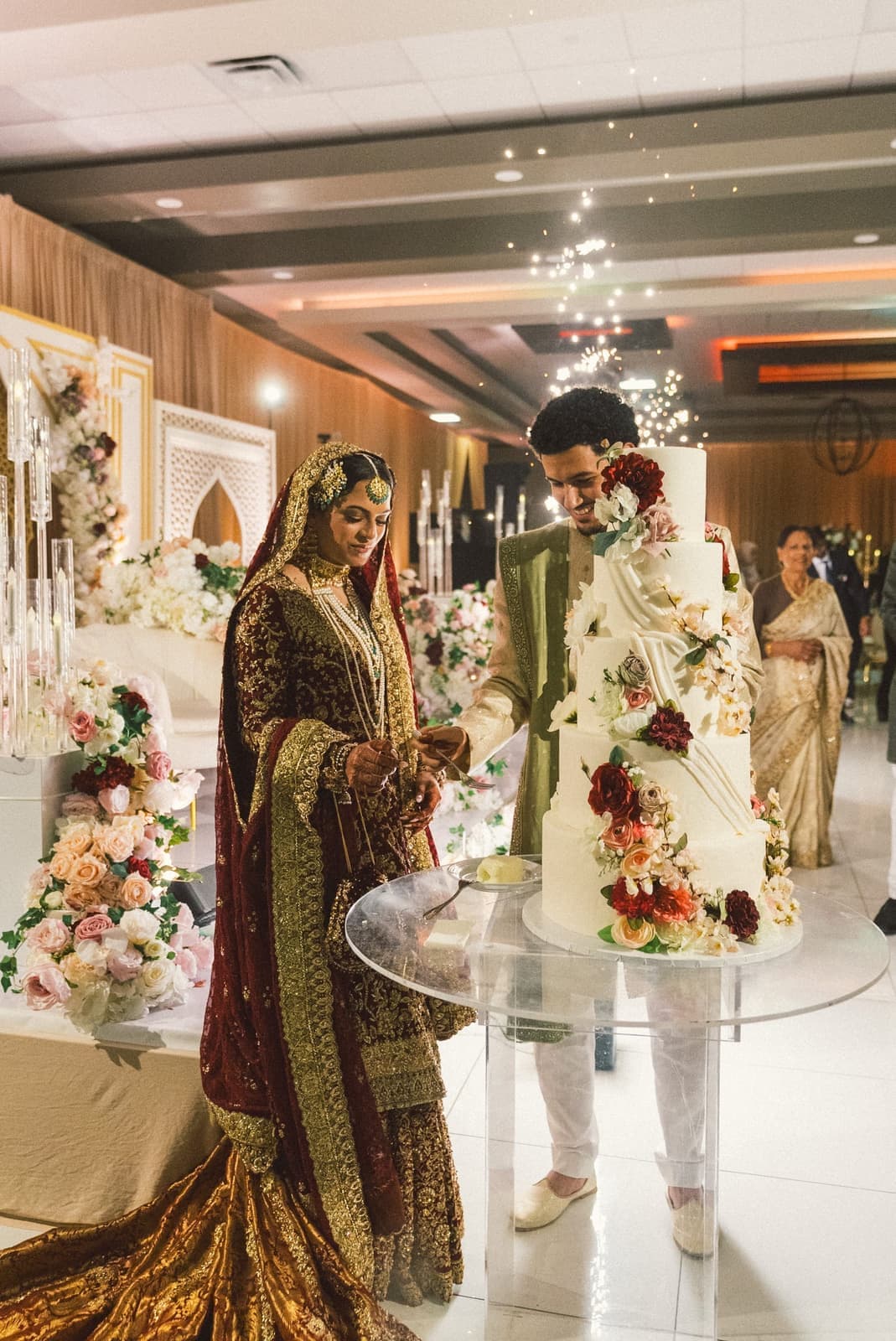 Couple cutting a floral wedding cake as sparkler fountains erupt behind them