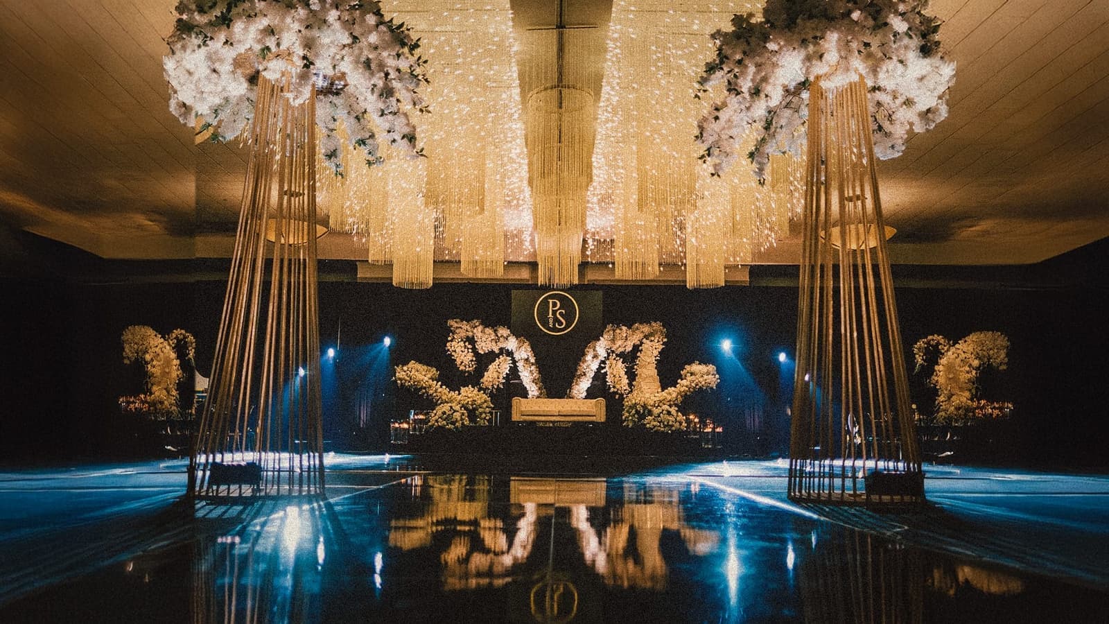 Reception stage with floral monogram backdrop and hanging gold chandeliers