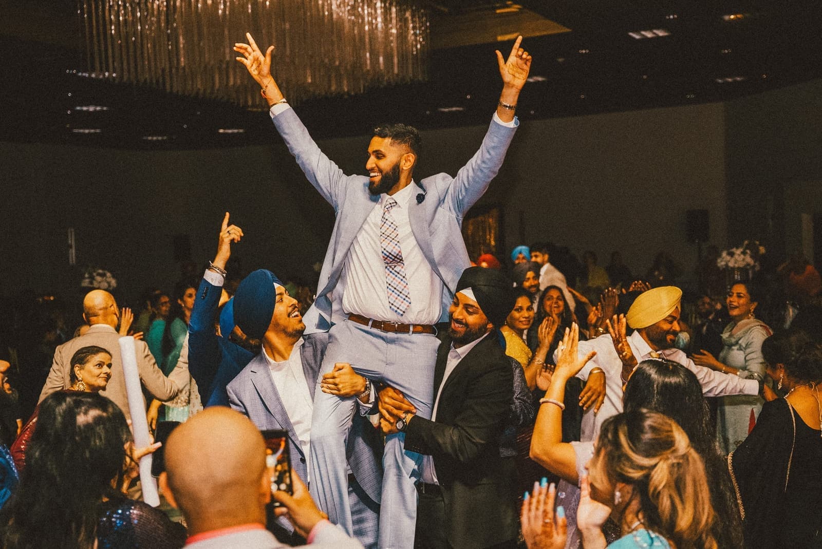 Groom lifted on friends shoulders with arms raised on the dance floor